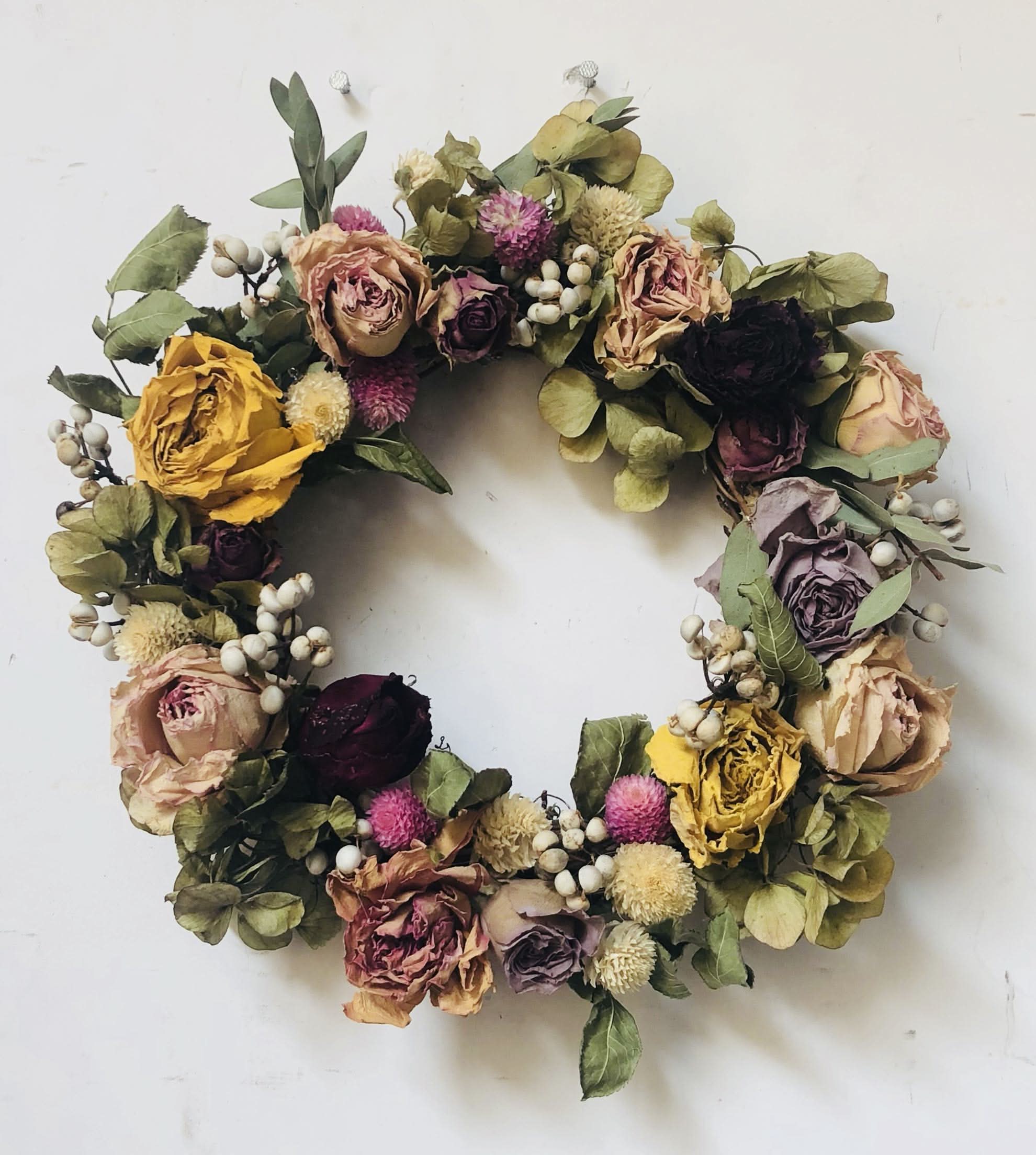 Natural Rose Round Garland: dried roses, eucalyptus, berries, and greenery on white wall.