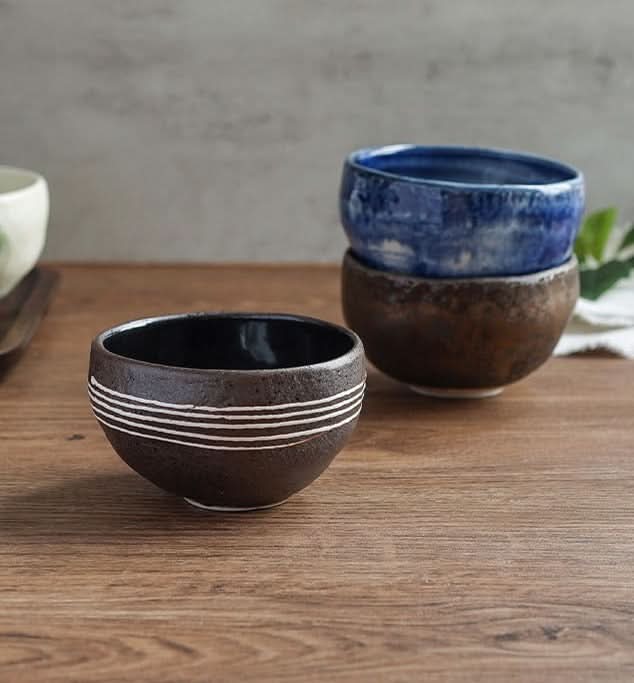Japanese imported Mino-yaki wedge-shaped matcha bowl in dark brown with white stripes on wooden table.