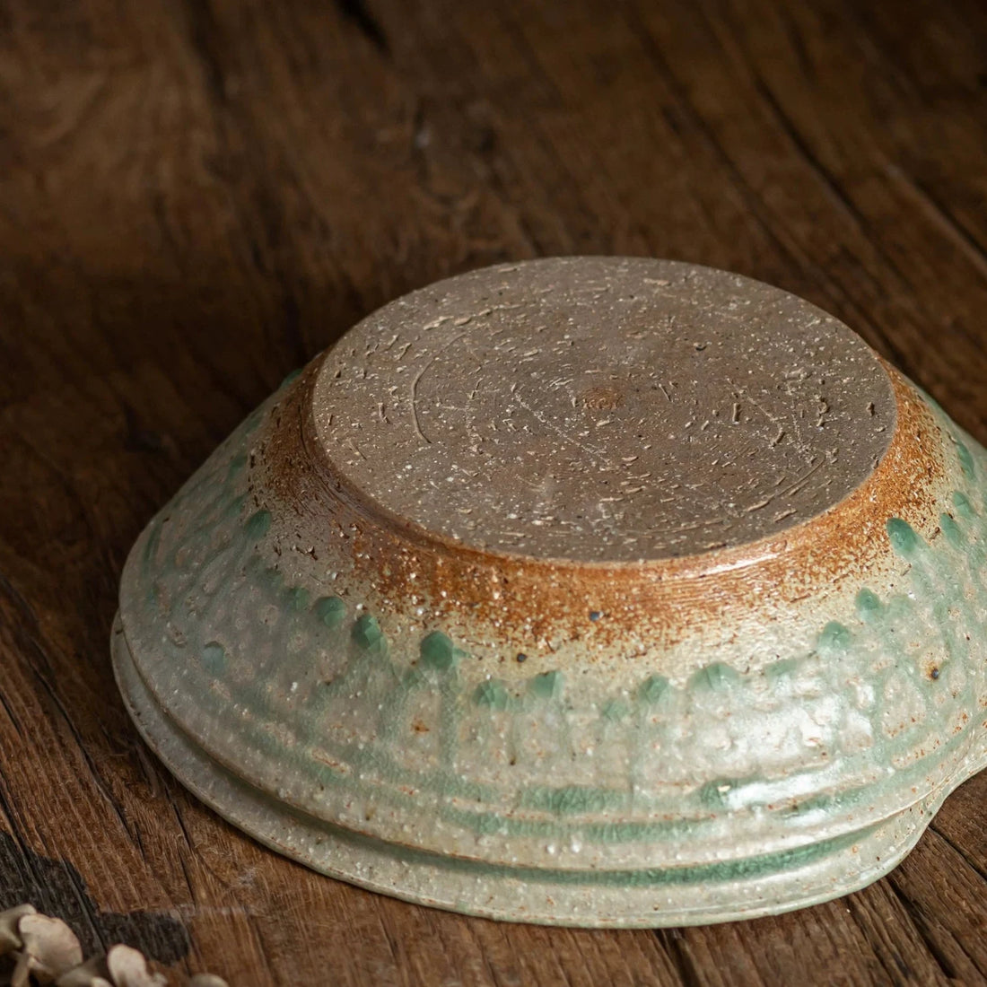 Underside view of a handmade ceramic bowl showing the unglazed reddish-brown foot and textured green rim.
