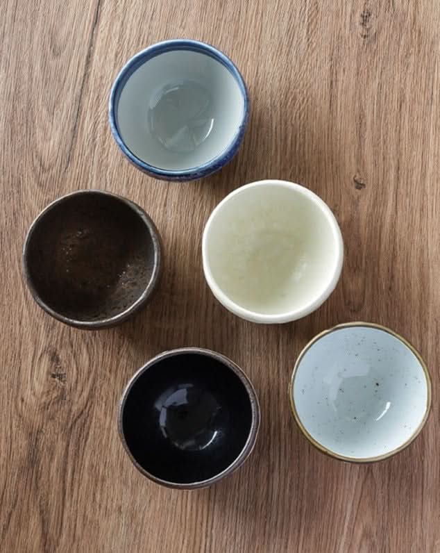 Mino-yaki wedge-shaped matcha bowls in assorted colors on a wooden surface.