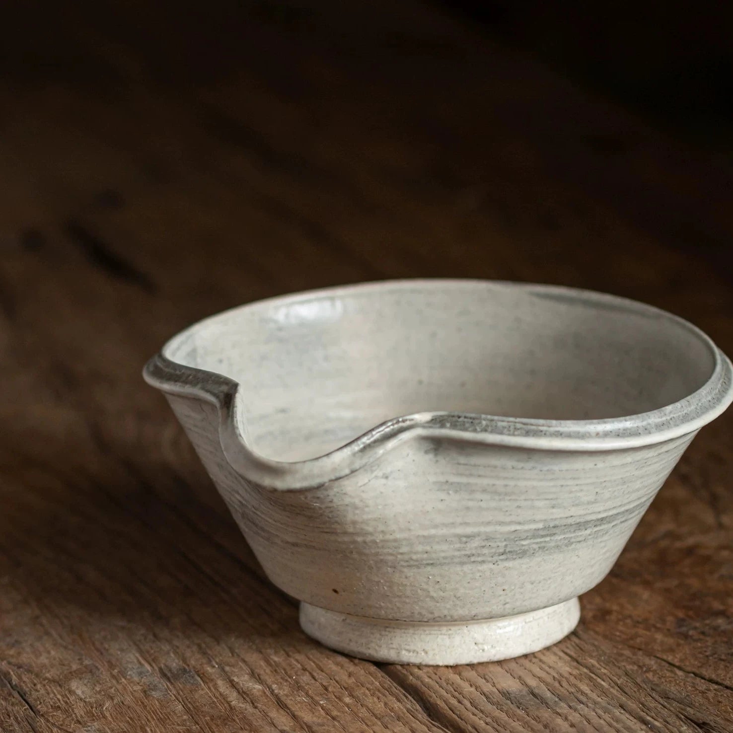 Side profile of a handmade ceramic bowl with a flared rim and a pronounced pouring spout, showing its depth.