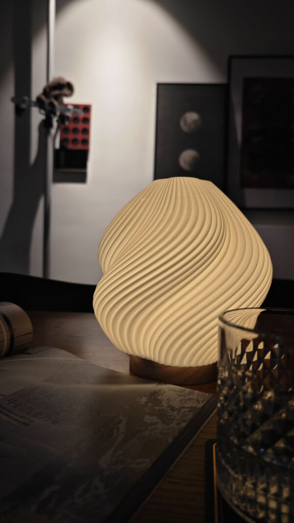 Whimsical Wave Table Lamp glows warmly on a wooden surface with a glass and book.