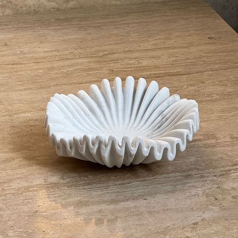 White carved marble fruit bowl with fluted design on a tan surface.