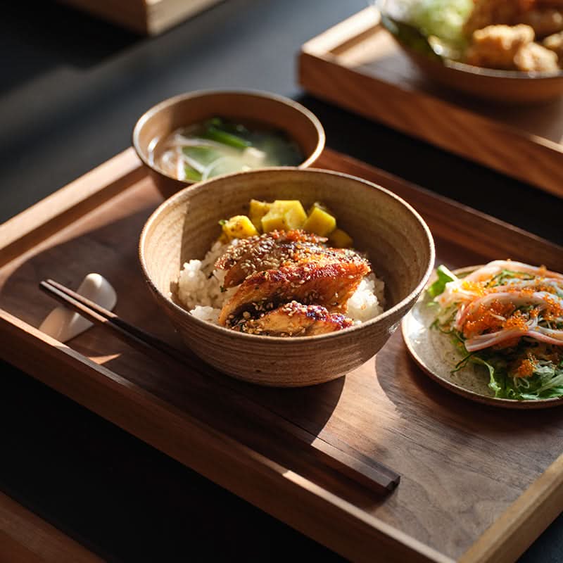 Brown clay tableware handmade set with rice bowl, soup, and salad on a wooden tray.