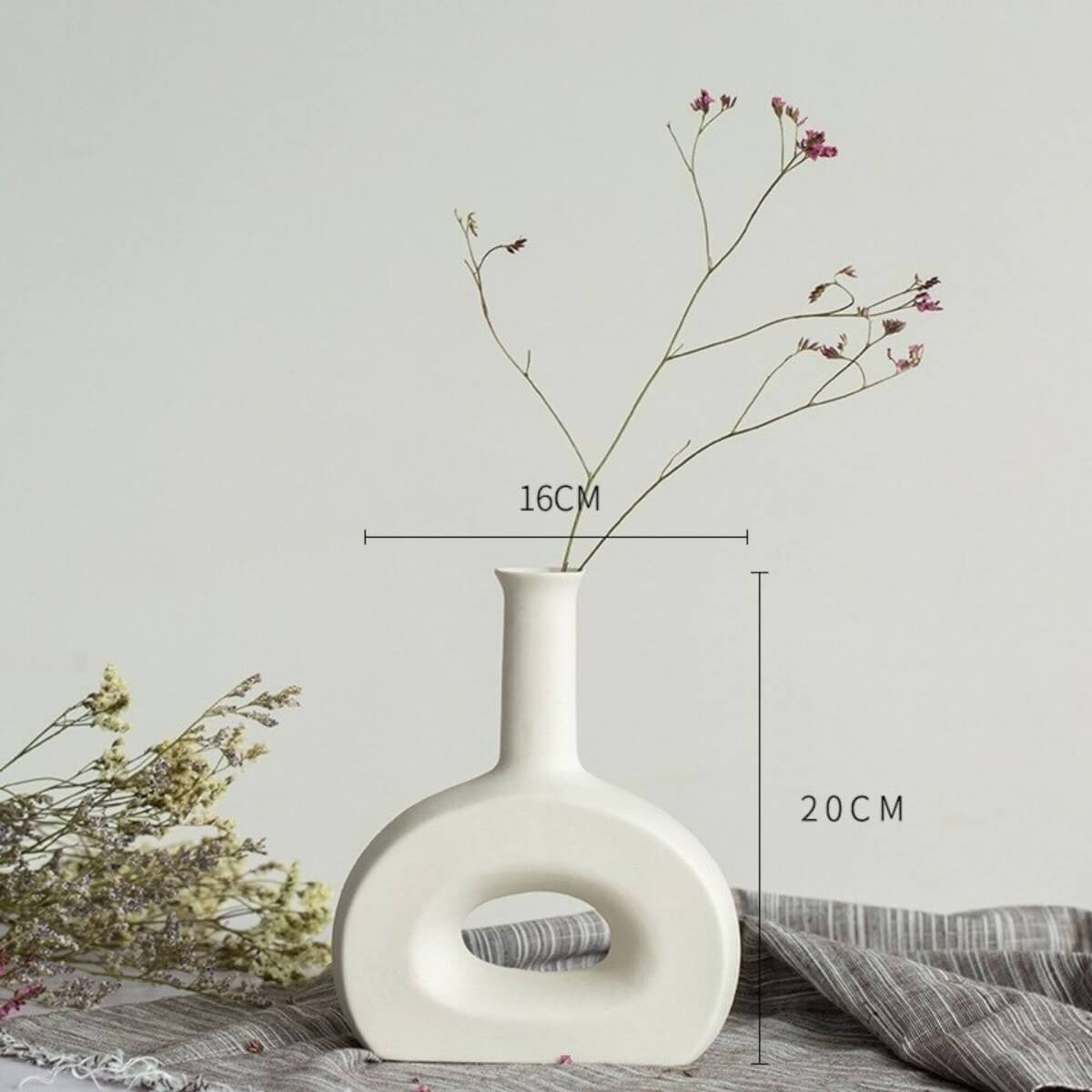 Abstract white vase with minimalist design, featuring dried flowers on a gray linen cloth.