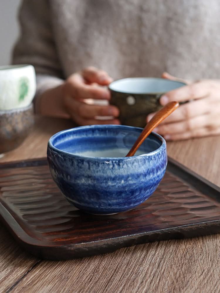 Blue Mino-yaki wedge-shaped matcha bowl with wooden spoon on textured tray.