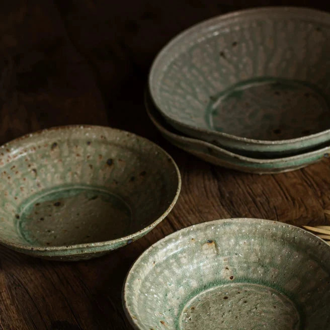 Three vintage-style ceramic bowls with textured green glaze displayed on a dark wood table.