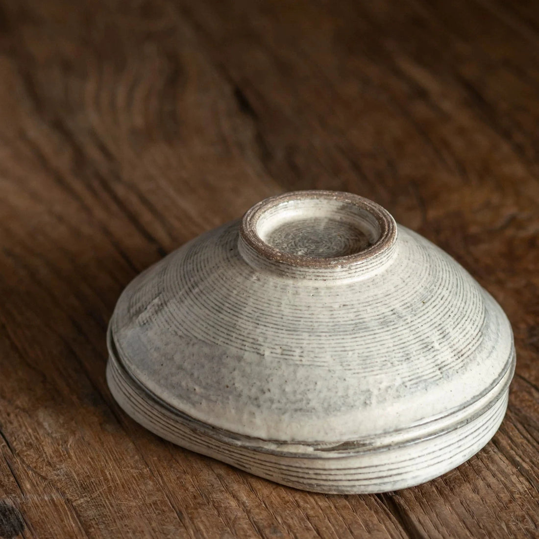 Ceramic bowl shown upside down, revealing the concentric rings and foot ring base on wood.