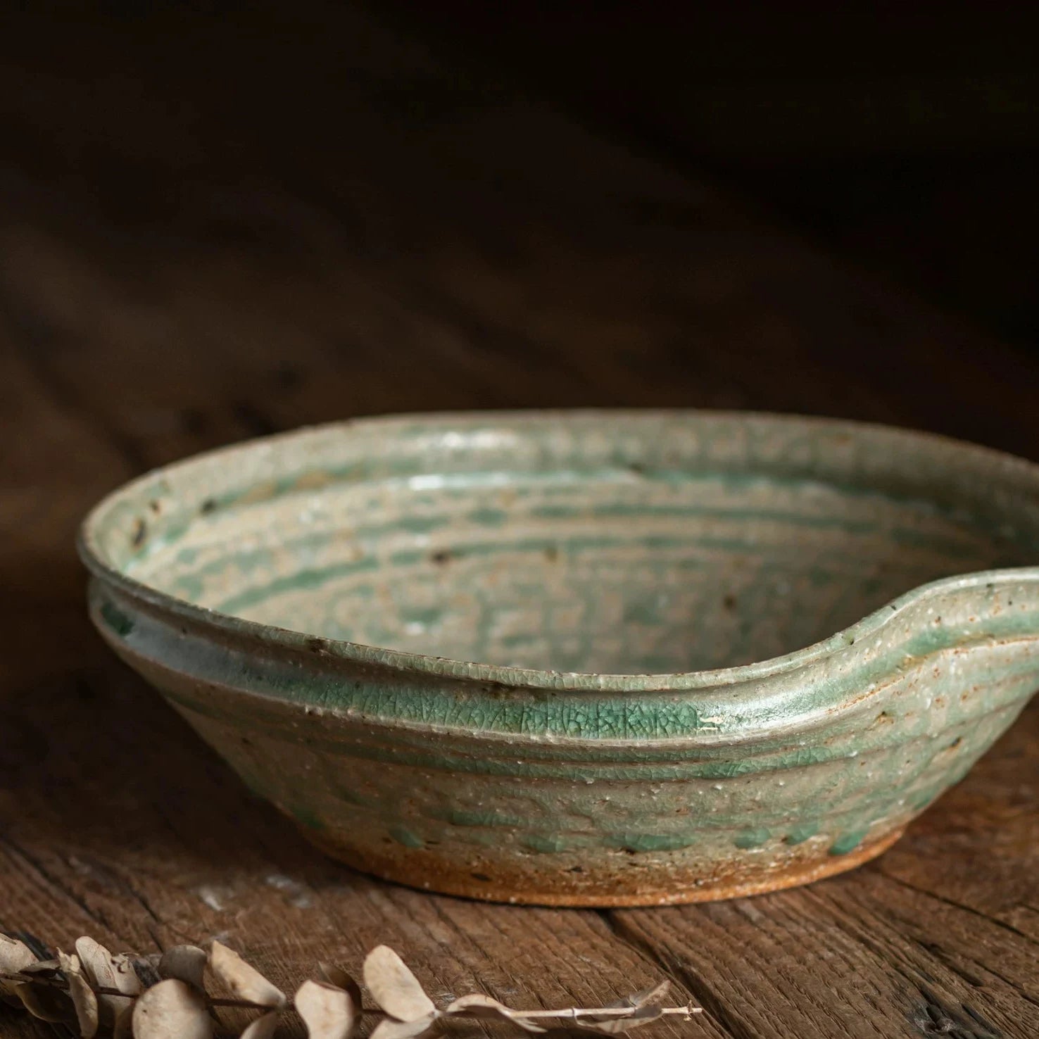 Close-up of a rustic, shallow ceramic bowl with a distinctive spout, featuring a mottled green glaze.