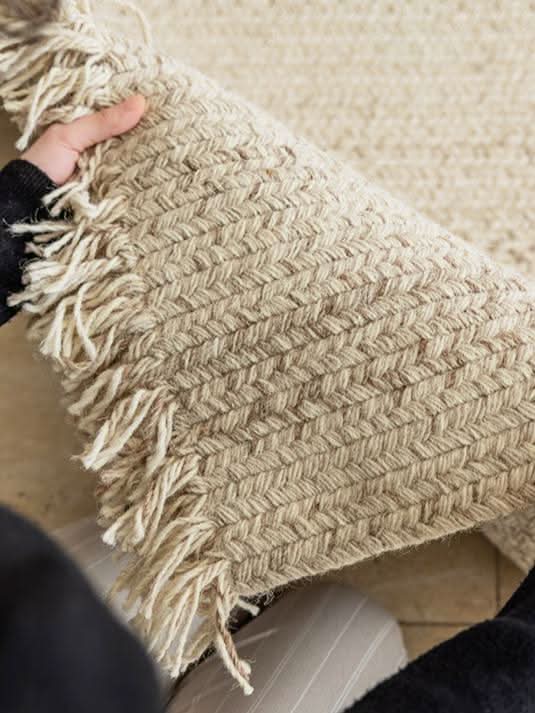 Close-up of a beige wool braided rug with fringe detail, showcasing the texture.