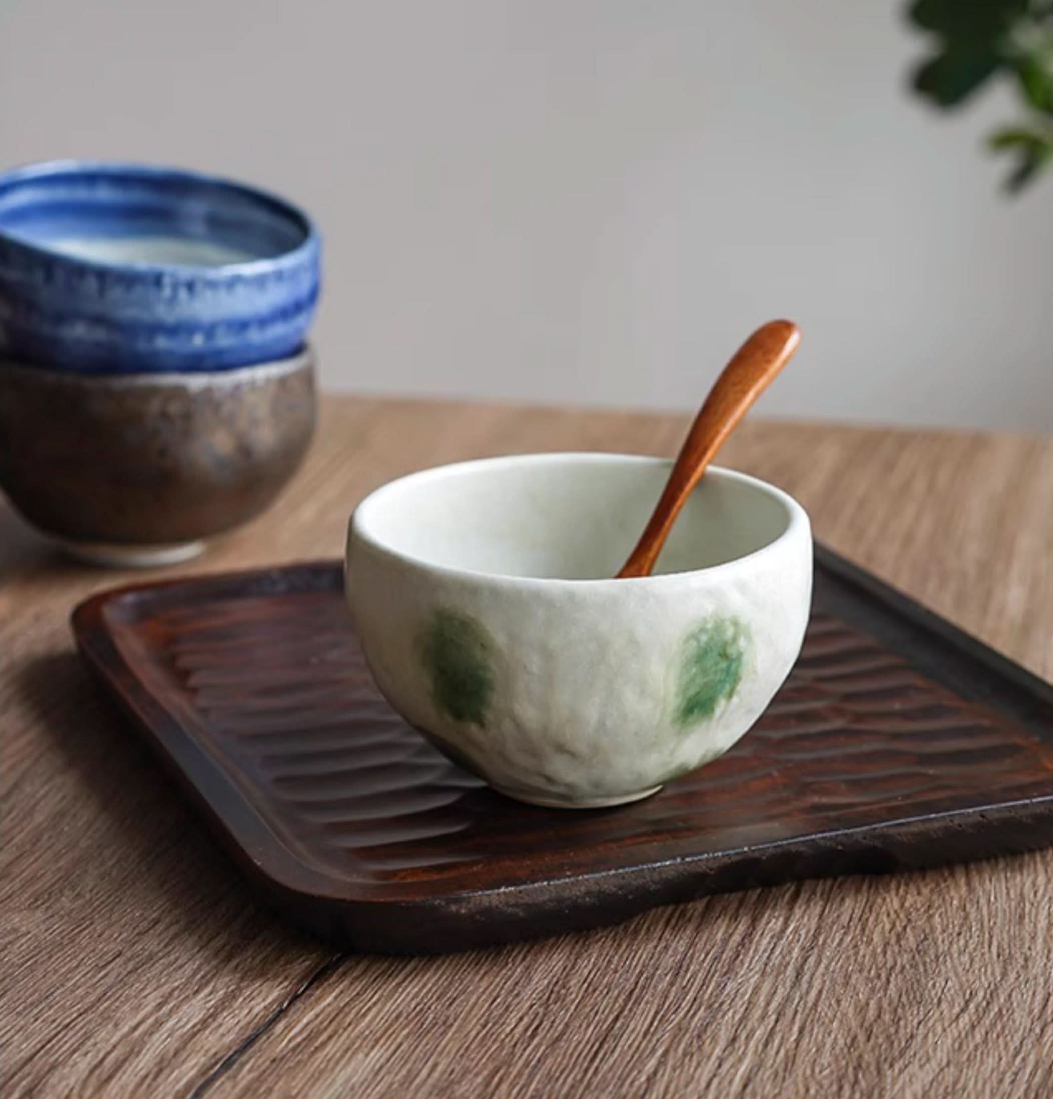 Japanese imported Mino-yaki wedge-shaped matcha bowl with green accents, on wooden tray.