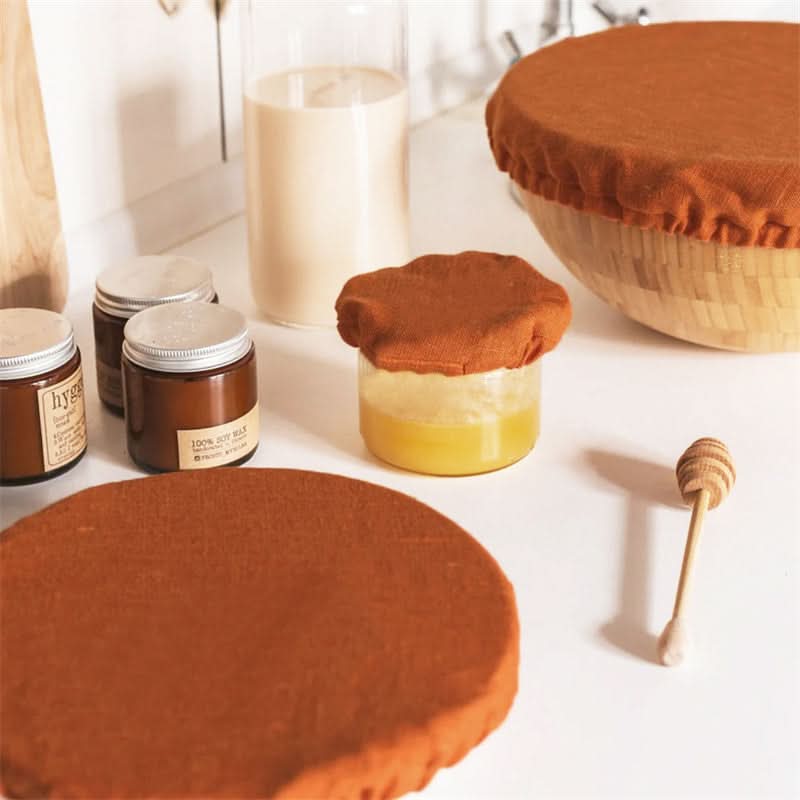 Orange linen bowl covers protect jars and bowls on a kitchen counter.