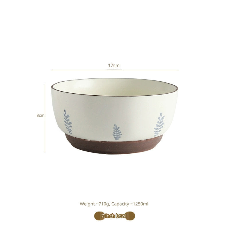 A white ceramic bowl with a brown base, decorated with small blue leafy branches. Dimensions are indicated as 17cm wide and 8cm tall.