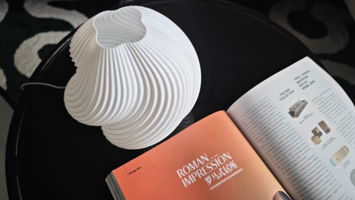 White 3D Printed Wave Design Creative Lamp on black table with open magazine.