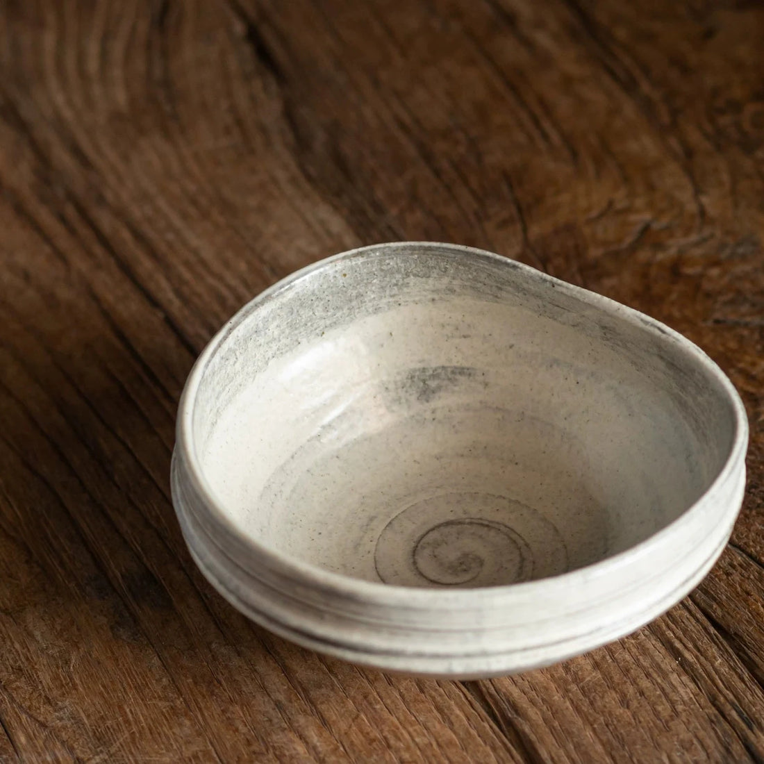 Handcrafted ceramic bowl with a slightly rippled, uneven rim on a warm wooden background.