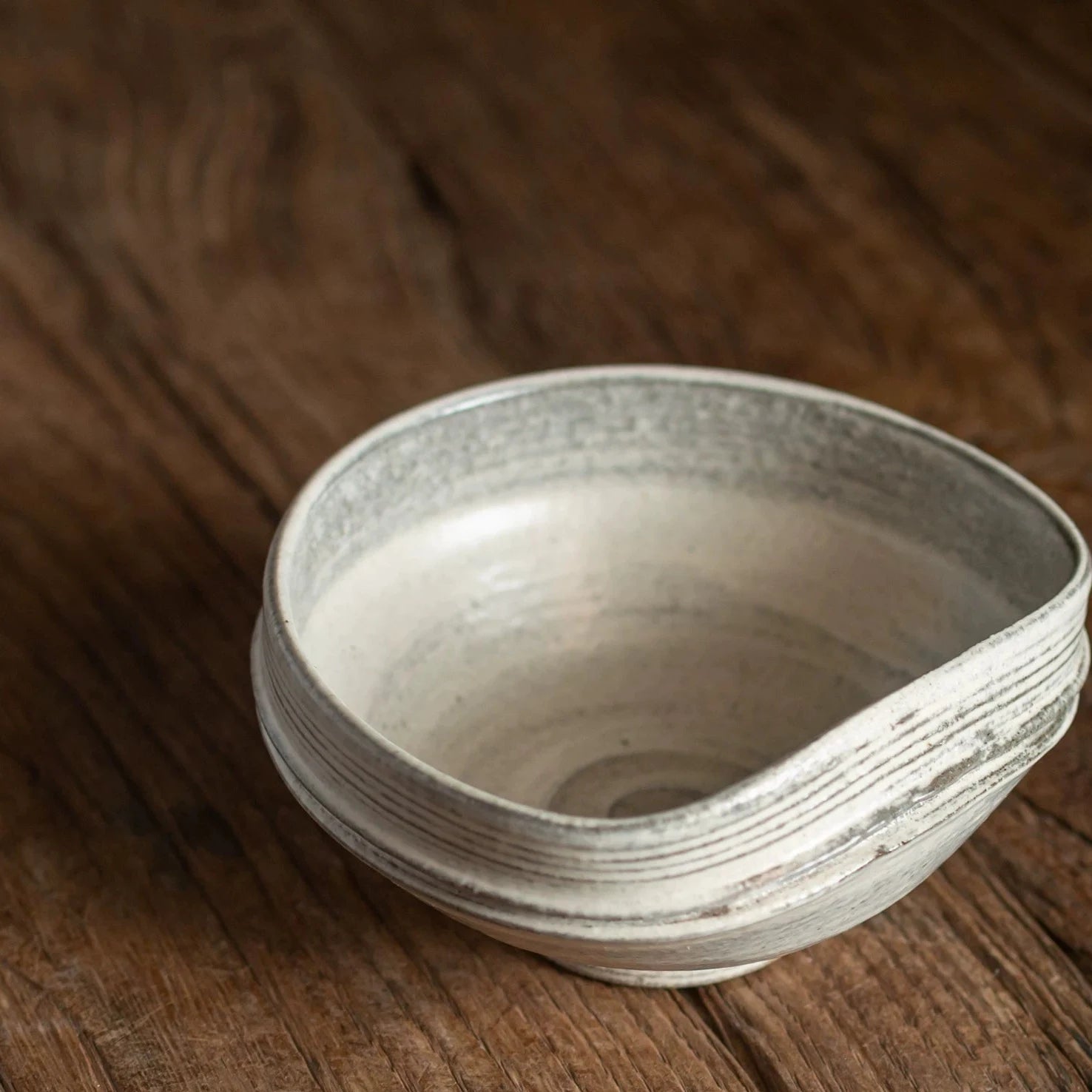 Close-up of a handmade ceramic bowl with an organic, uneven rim resting on a dark wooden surface.