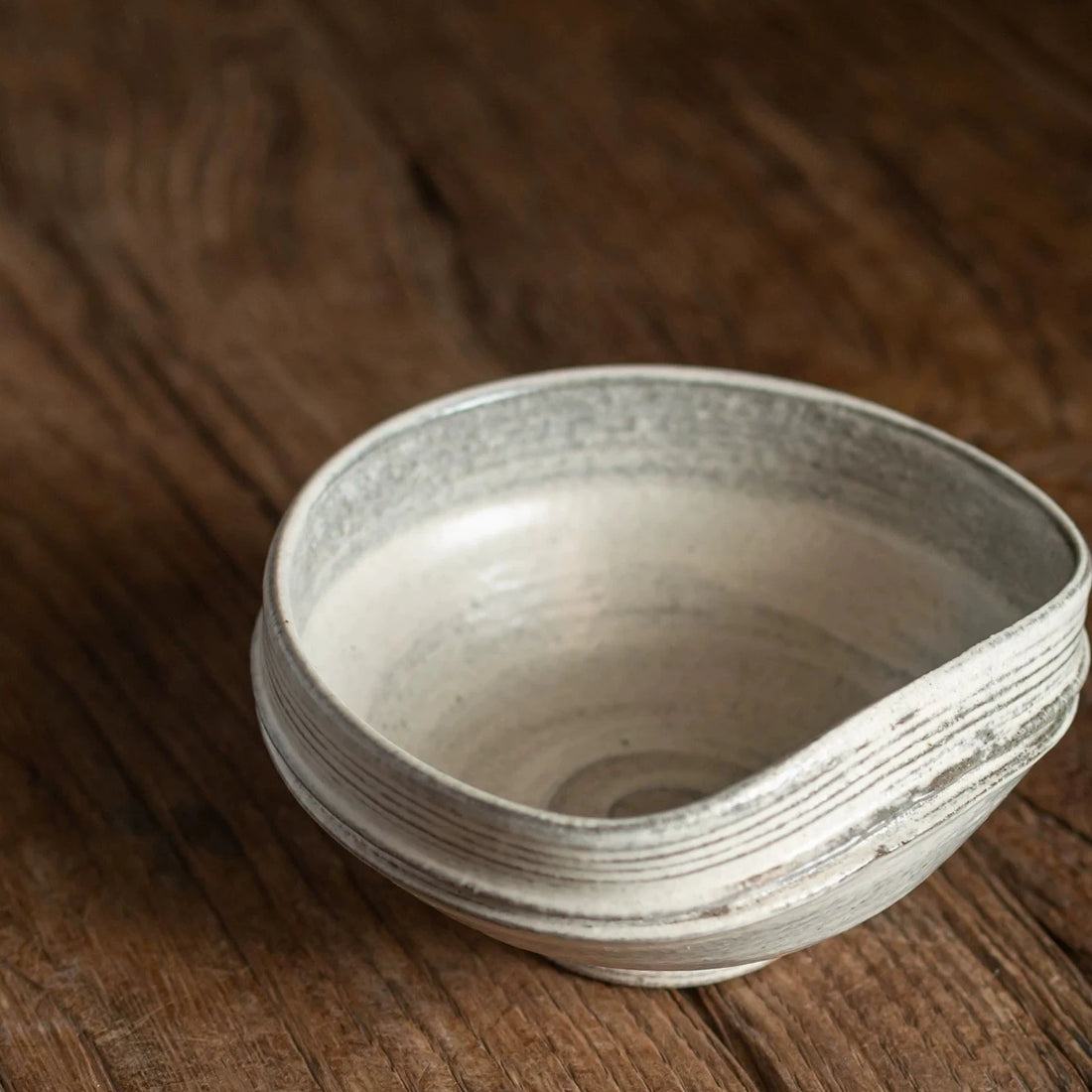 Close-up of a handmade ceramic bowl with an organic, uneven rim resting on a dark wooden surface.