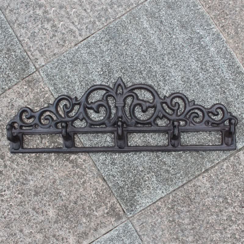 Black ornate cast iron outdoor wall hanger on textured stone tiles.