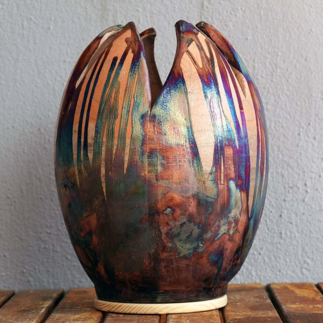 Large, colorful flower-shaped ceramic vase with unique raku firing patterns.  Multi-colored,  oval shape.  On wooden base.