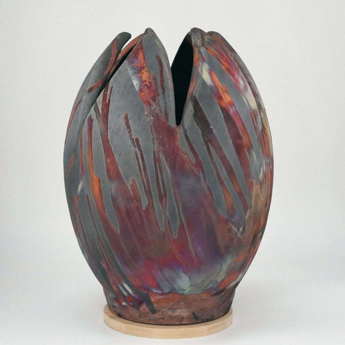 Large, colorful flower-shaped ceramic vase; raku firing; unique design; wooden base.