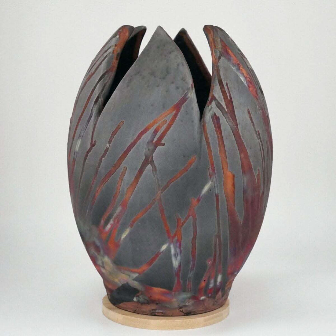 Large, gray-and-red ceramic flower vase with unique raku firing design; tulip-shaped; on wooden base.