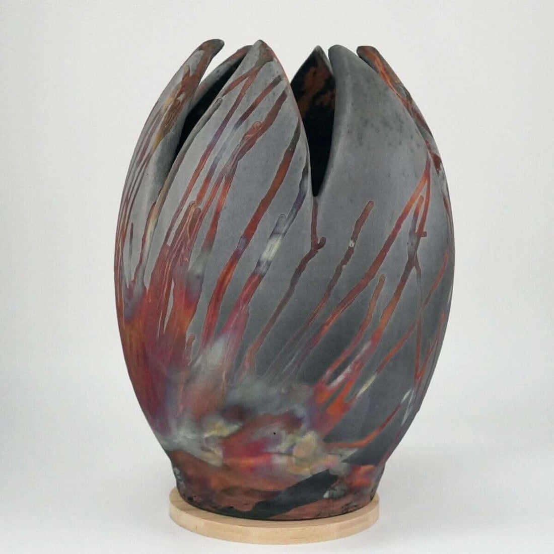 Large, tulip-shaped ceramic vase with raku firing; grey, red, and multicolored design; wooden base.