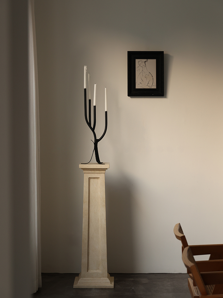 Modern Branch Candle Holder in black metal with white candles on a stone pedestal.