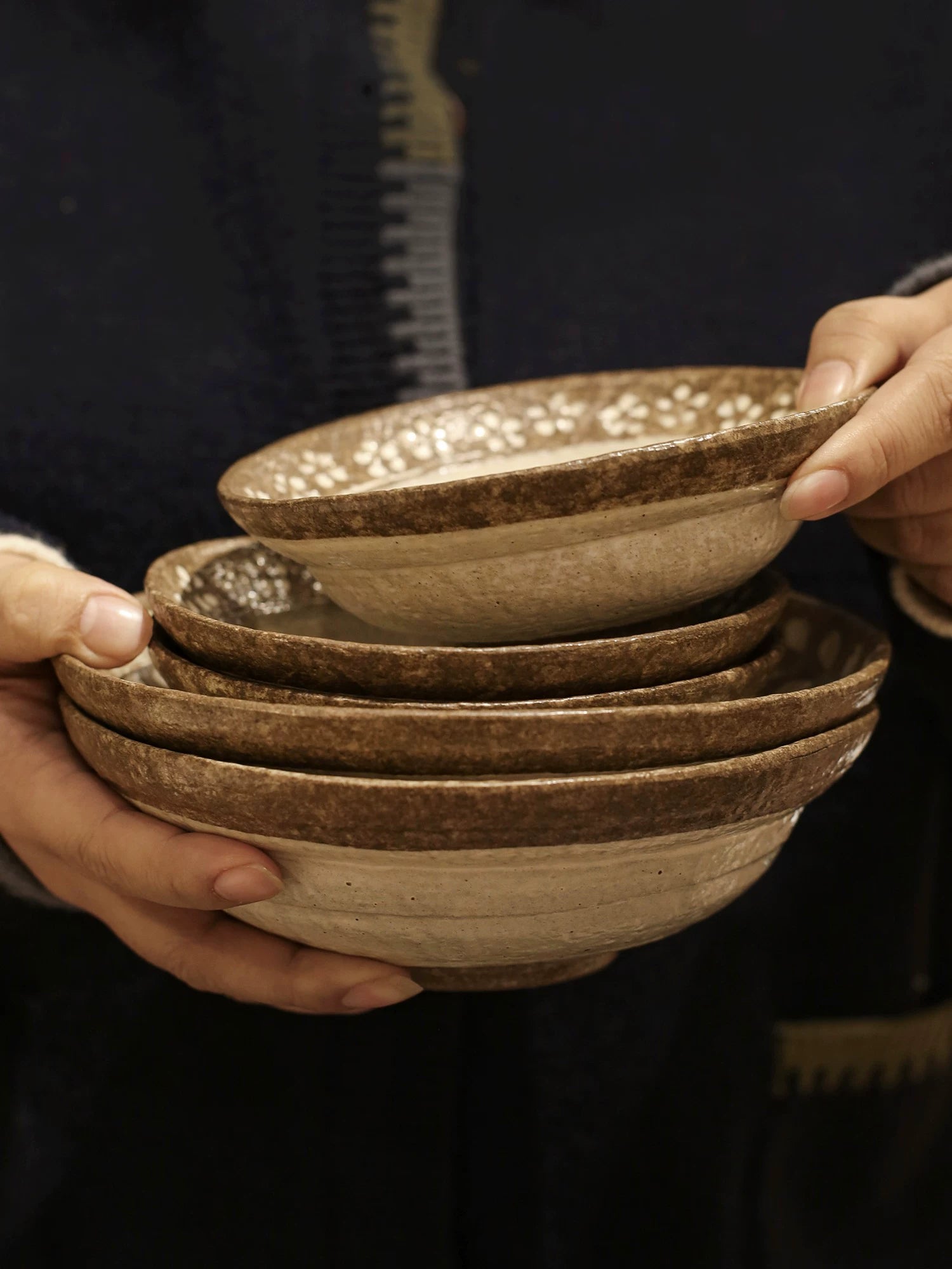 Hands holding a stack of three small rustic ceramic rice bowls with brown floral rim.