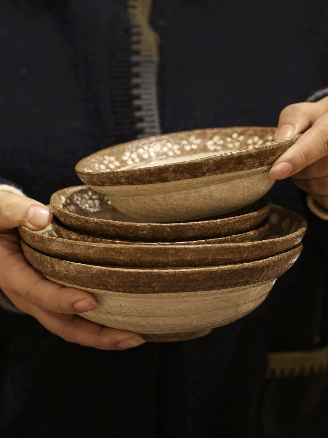 Hands holding a stack of three small rustic ceramic rice bowls with brown floral rim.