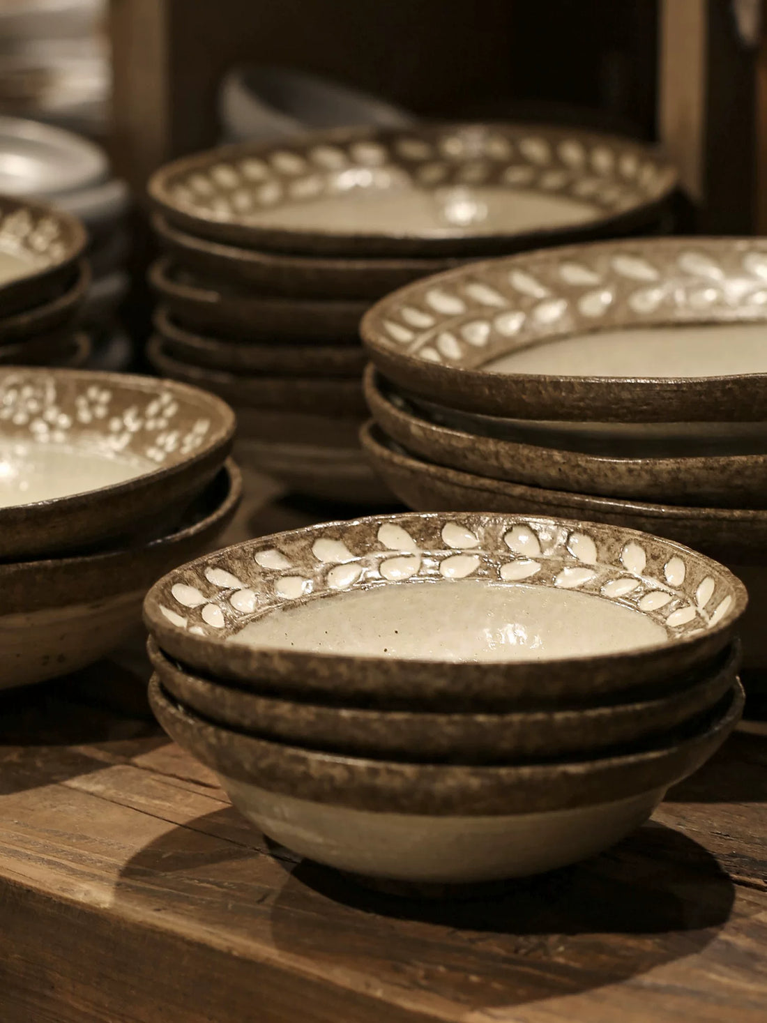 Stack of three rustic ceramic noodle bowls (7-inch) with brown floral pattern on a wooden surface.