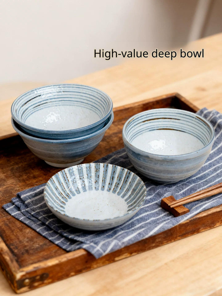 Assortment of Japanese style ceramic bowls and a small dish on a wooden tray with a blue striped cloth.