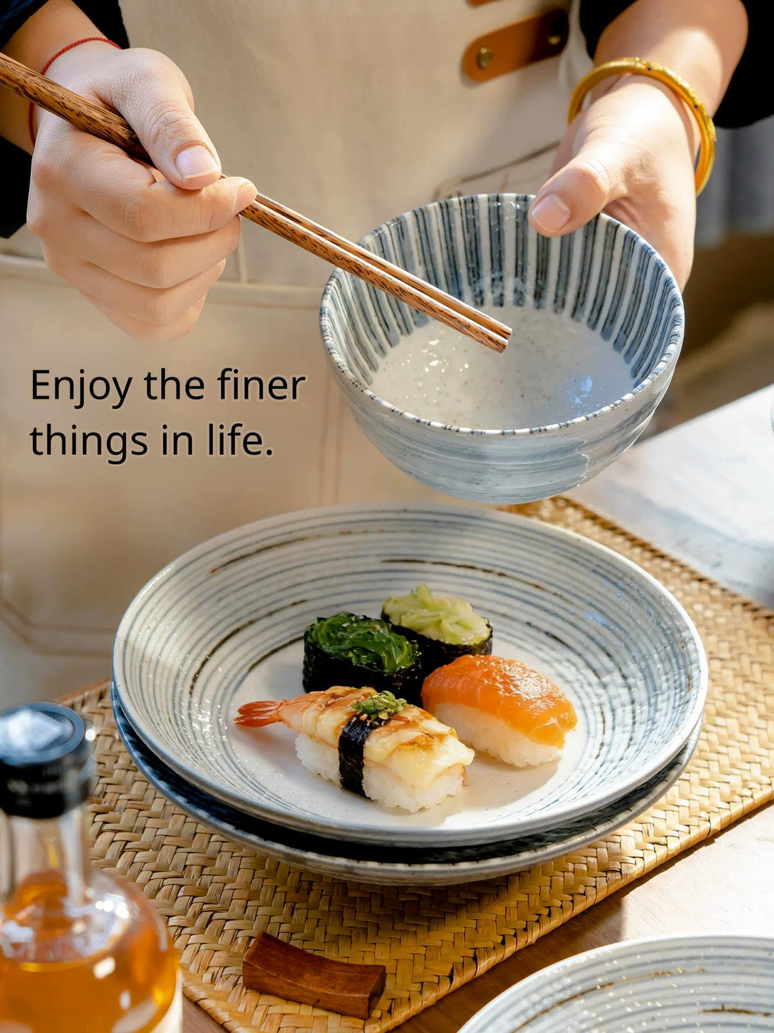 Hands holding a Japanese style striped bowl over a set of stacked striped plates with sushi pieces.