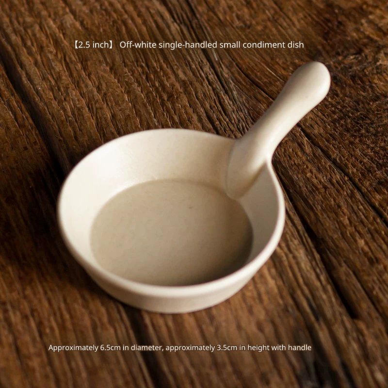 Small, round, cream white ceramic sauce or dipping dish with a small handle, 6.5cm diameter.
