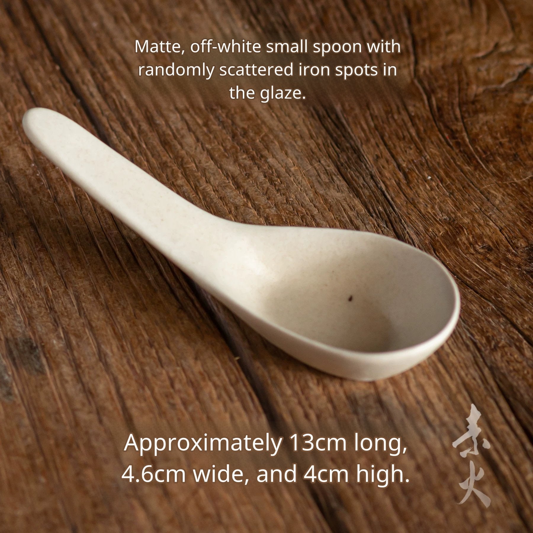 Long-handled white ceramic soup spoon with speckles on a dark wood background, 13cm long.