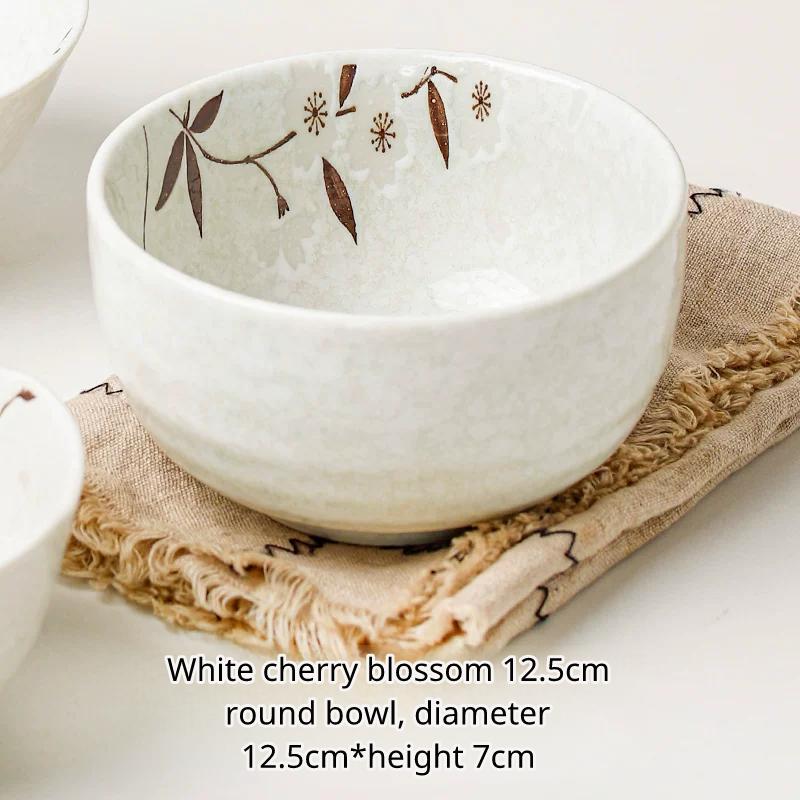 Medium white ceramic round bowl with brown cherry blossom pattern resting on a textured cloth.