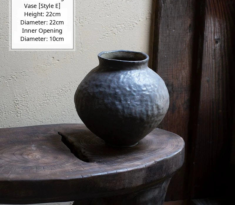 A handmade black glossy ceramic vase with an organic, asymmetric shape sits against a plain background.