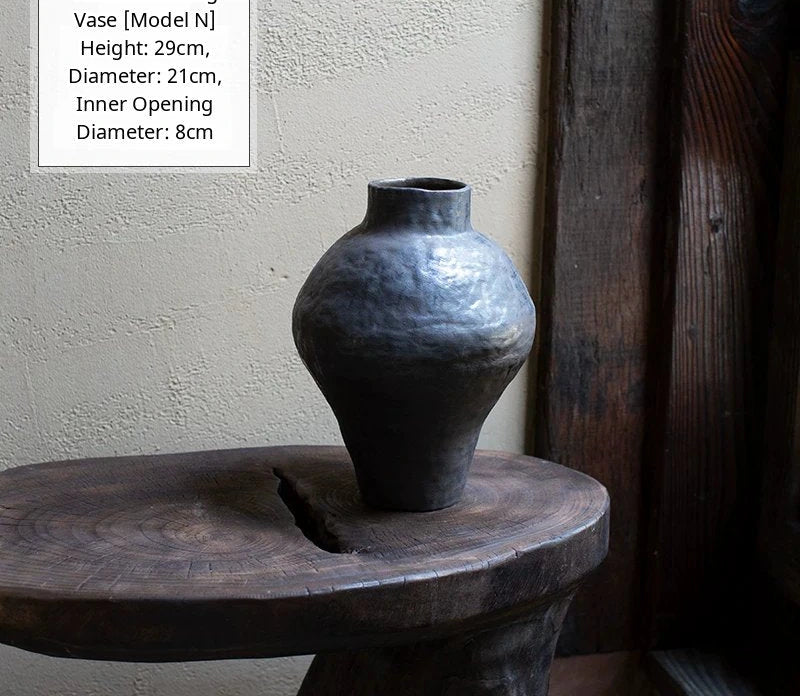 A handmade black glossy ceramic vase with an organic, asymmetric shape sits against a neutral background.