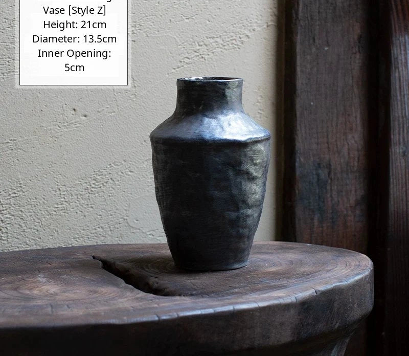A black glossy handmade ceramic vase with an irregular, wavy silhouette on a neutral surface.