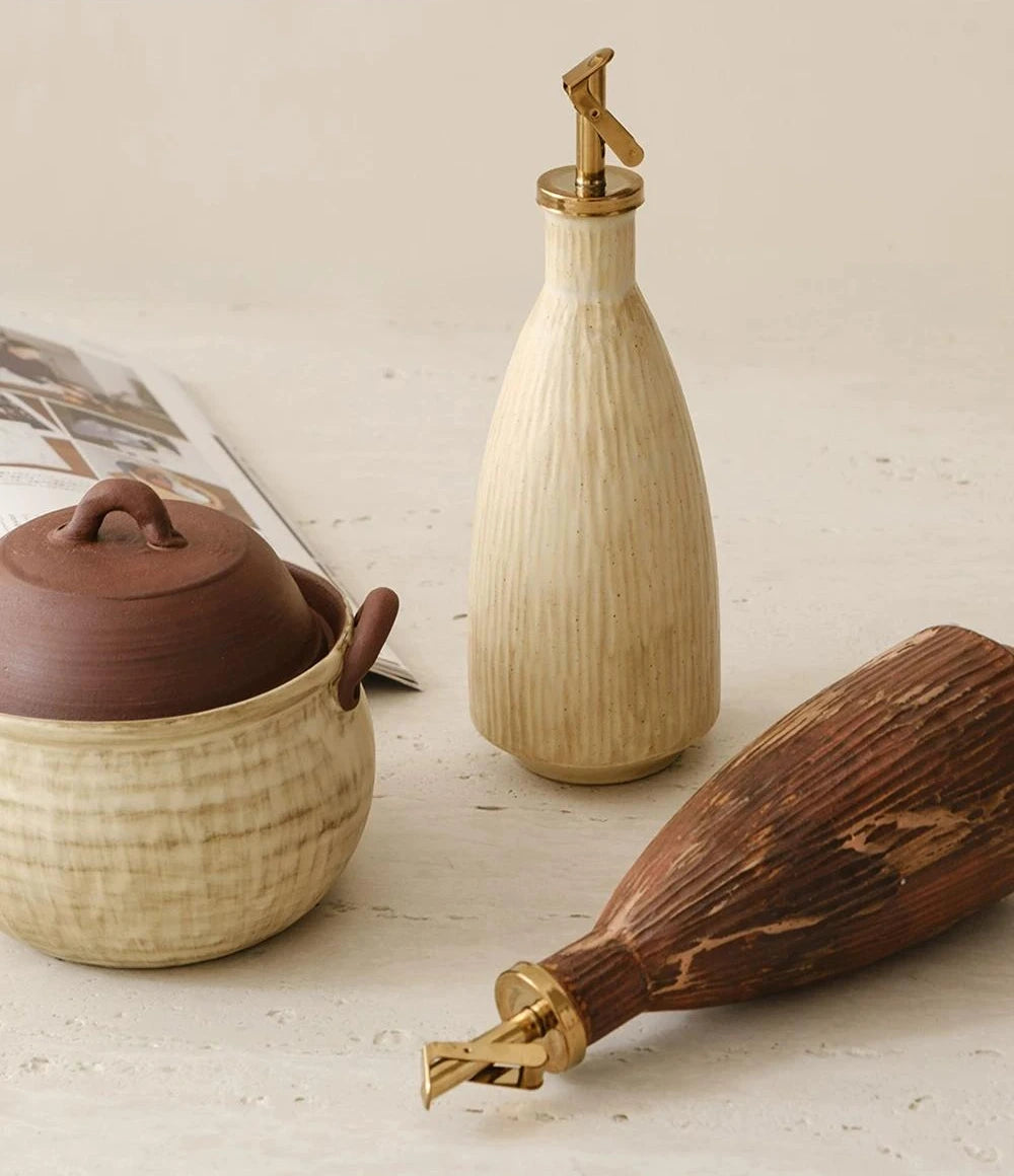A textured ceramic oil dispenser with a curved handle and an automatic flip metal spout.