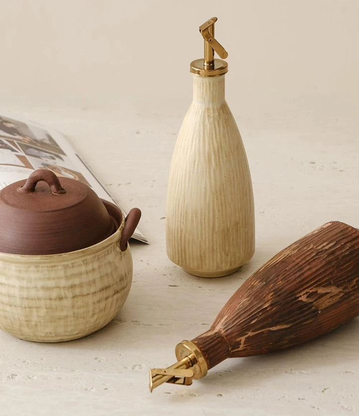 A textured ceramic oil dispenser with a curved handle and an automatic flip metal spout.