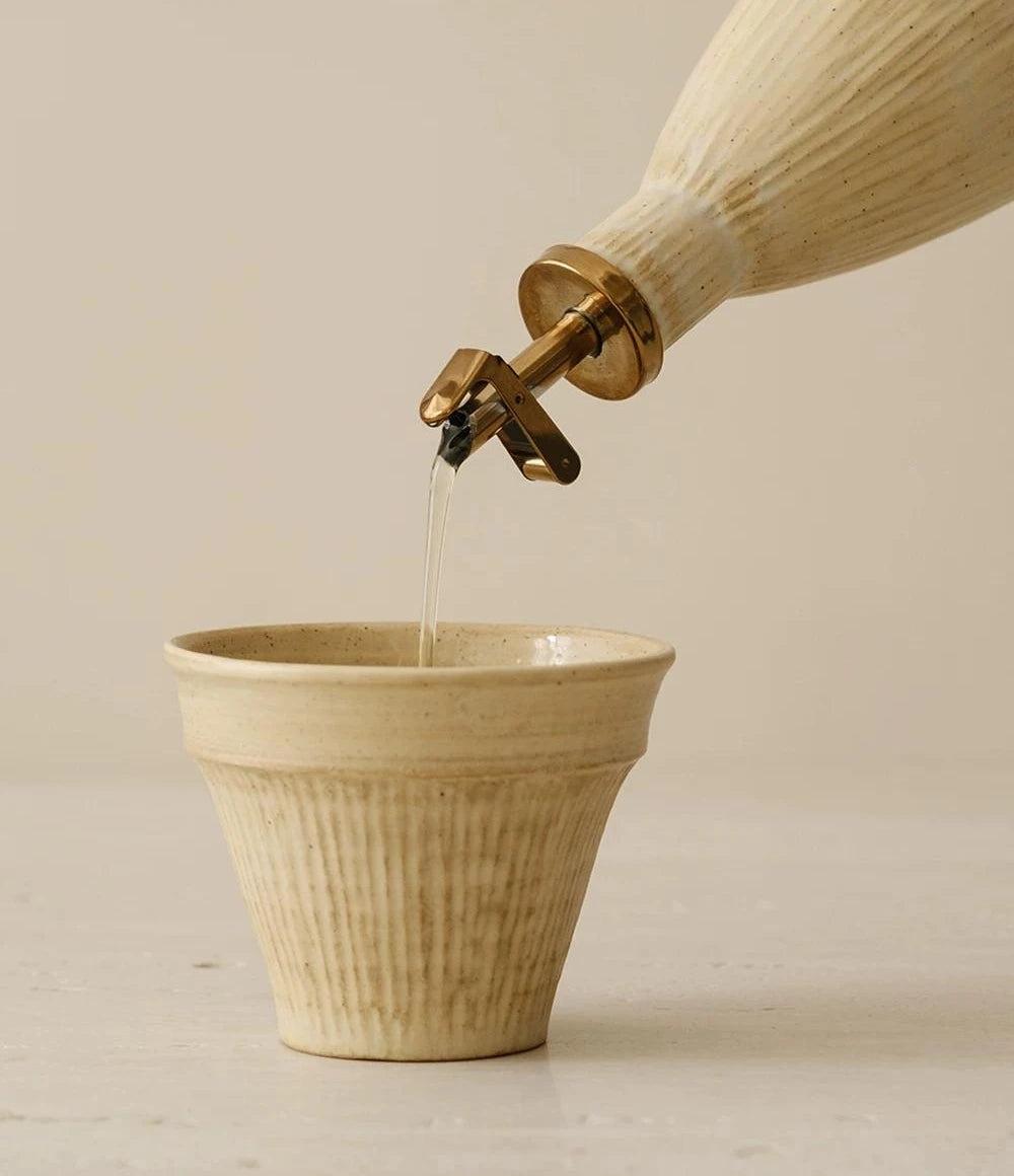 A textured ceramic oil dispenser with a curved handle and a metallic flip-top spout.