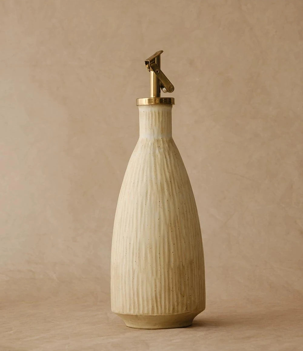 A cream-colored ceramic oil dispenser with a textured glaze and a silver automatic flip spout.