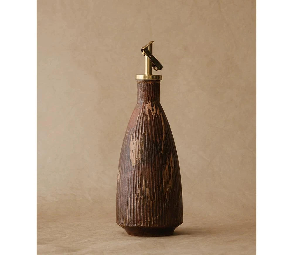 A textured ceramic oil dispenser with an automatic flip metal spout against a white background.