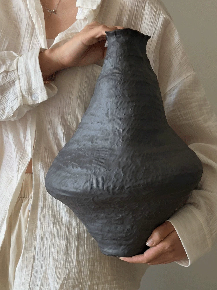 A handmade black ceramic vase with a textured clay finish and an artistic sculptural design.