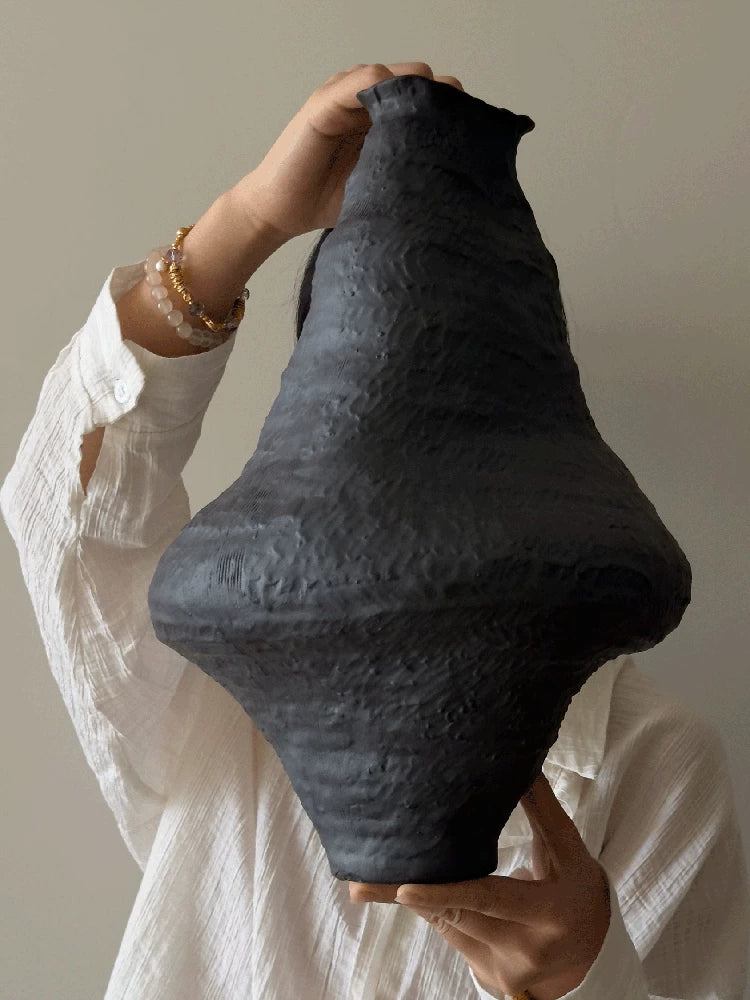 A handmade black ceramic vase with a textured clay finish and a sculptural, artistic shape.