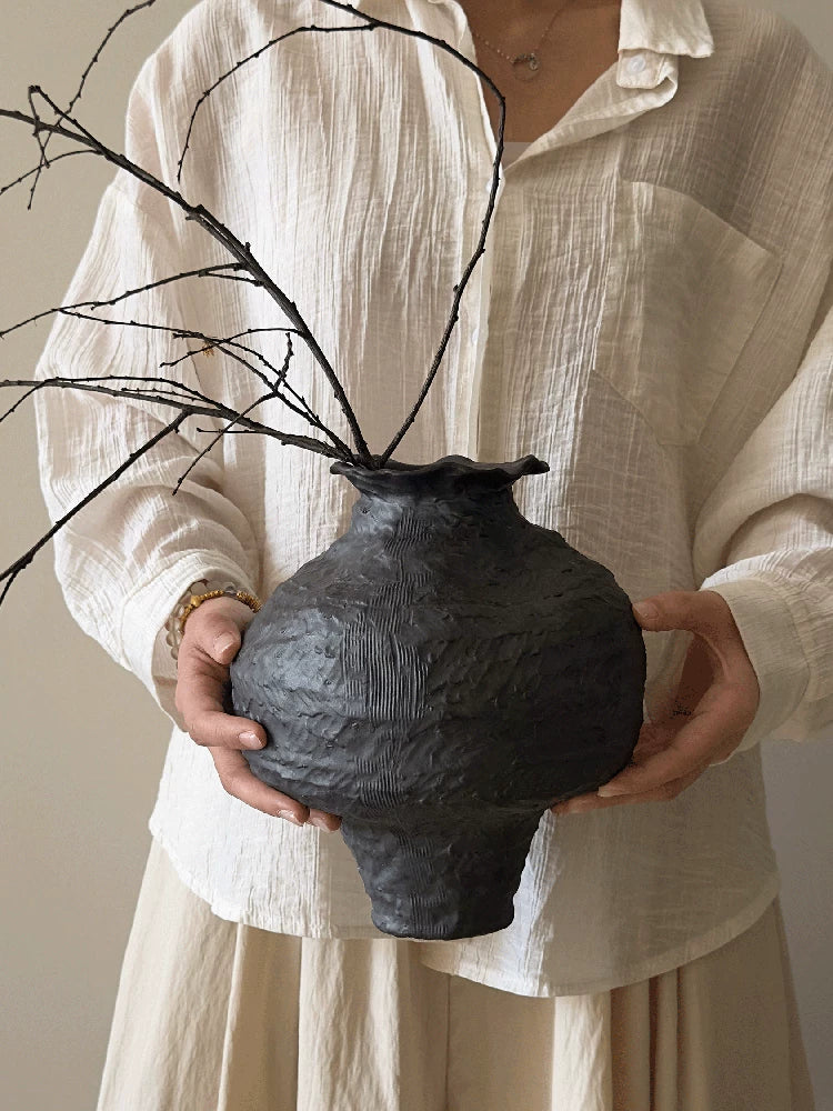 A handmade black ceramic vase with a textured clay finish and an artistic sculptural design.