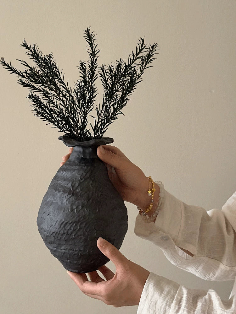 A handmade black ceramic vase with a textured clay finish and an artistic sculptural design.
