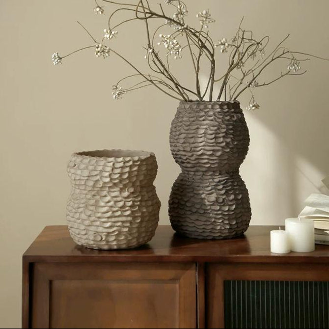 A rustic, textured ceramic vase with a tapered neck and neutral earthy finish.