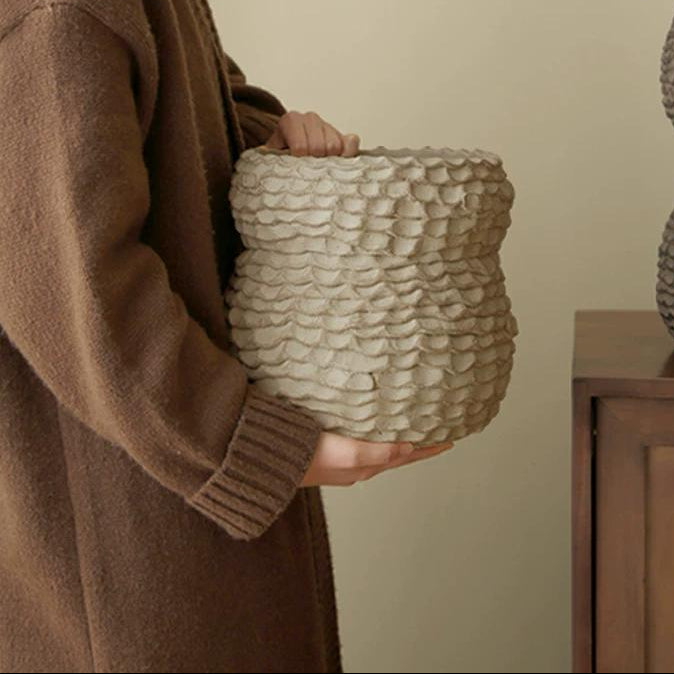 A handmade ceramic vase with a textured, rough pottery finish on a neutral surface.