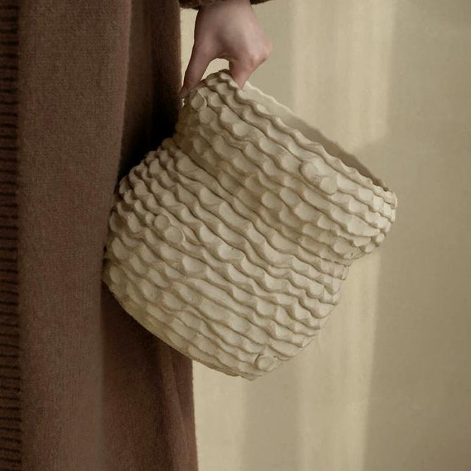 Handmade ceramic vase with a textured, rough pottery finish on a neutral surface.